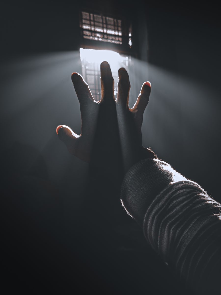 Eine Hand greift dem Licht durch ein Fenster entgegen