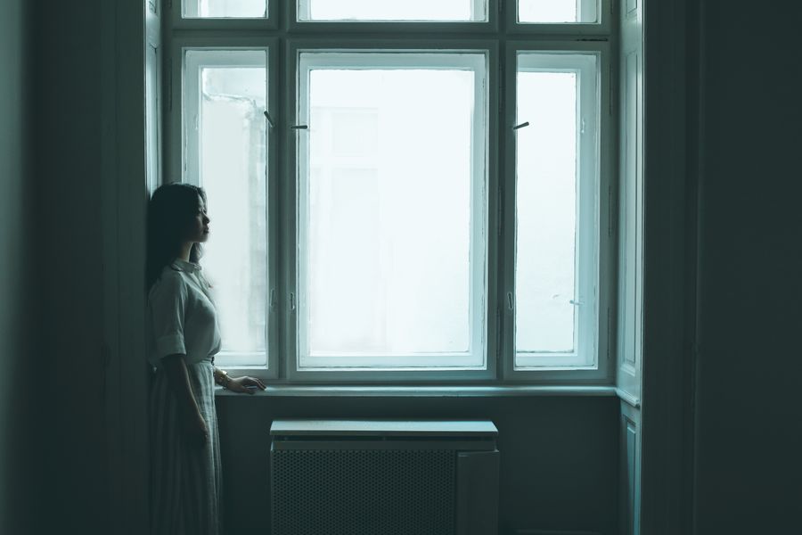 Person steht nachdenklich am Fenster
