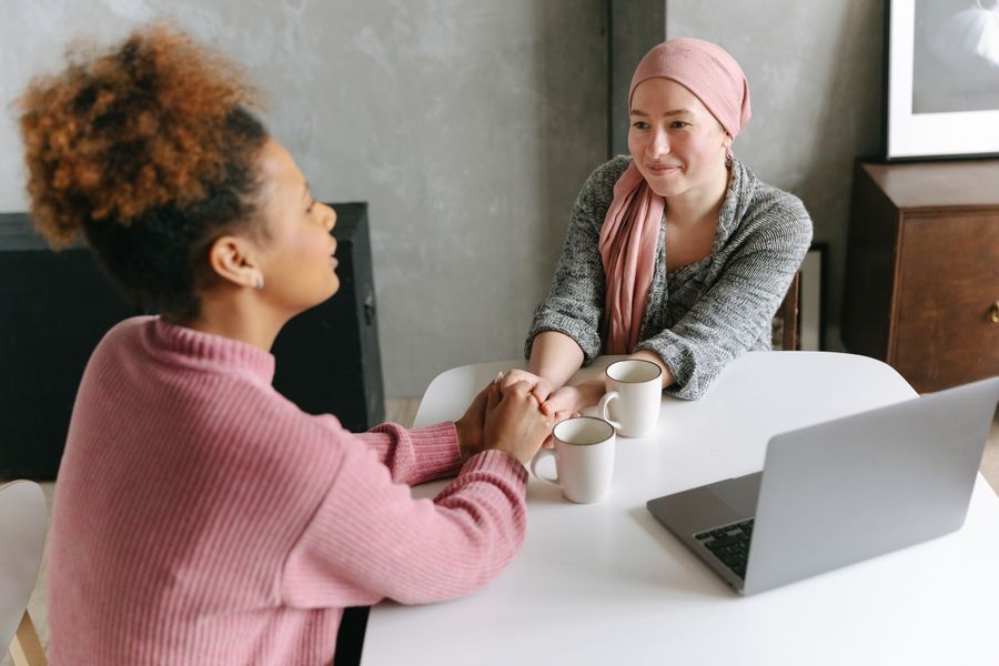 Zwei Frauen sitzen an einem Tisch, eine hält der anderen die Hand